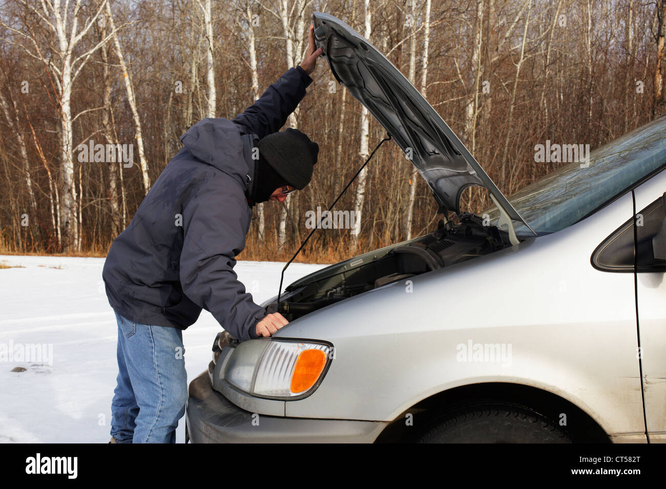 Uomo che guarda sotto il cofano di un veicolo in inverno. Foto Stock
