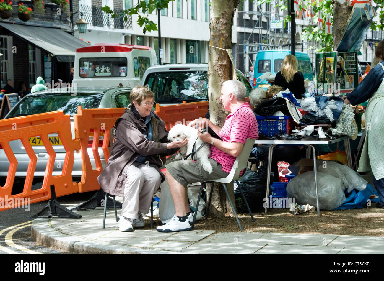Coppia con il loro piccolo cane bianco seduti su sedie sul marciapiede a Queen Square Fair, Bloomsbury Londra Inghilterra REGNO UNITO Foto Stock
