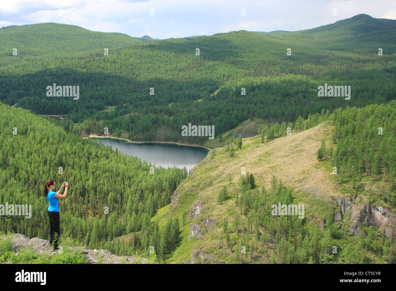 Donna prendendo foto del lago di montagna circondato da incontaminata foresta di pini, Altai, Siberia, Russia Foto Stock