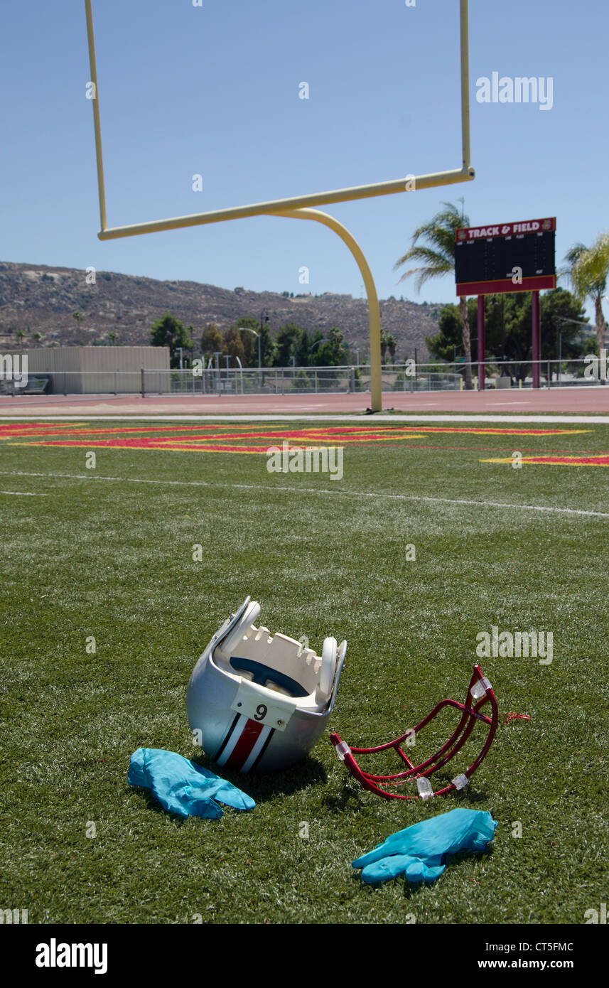 Conseguenze di un duro affrontare. Un casco da football americano, giace sul campo con maschera facciale strappato. I guanti chirurgici sono in vista. Foto Stock