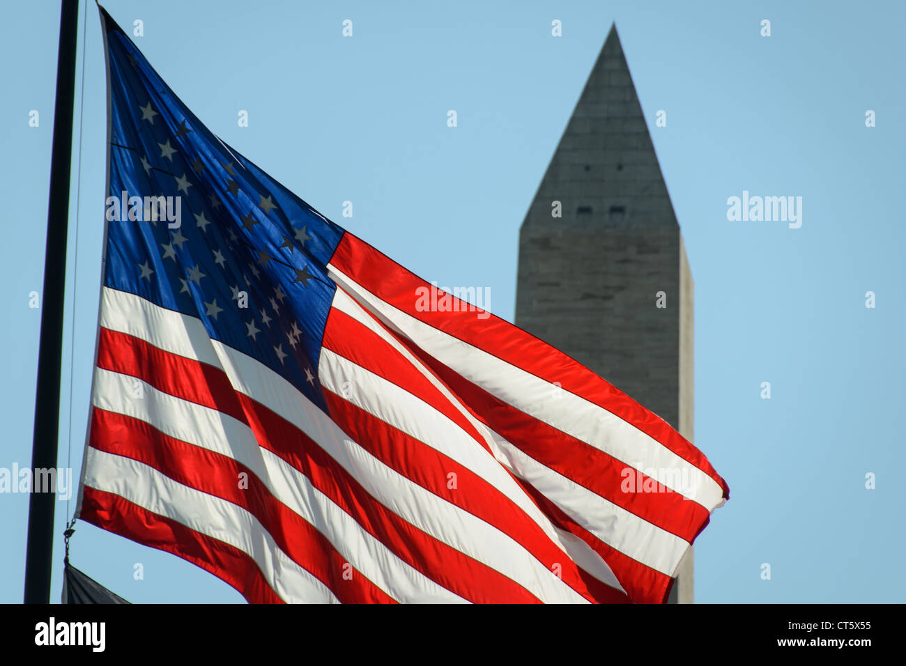 WASHINGTON DC - una bandiera americana vola in primo piano, retroilluminata contro il cielo, con la caratteristica forma a obelisco del monumento a Washington visibile sullo sfondo. Il monumento alto 555 metri, completato nel 1884, onora il primo presidente della nazione, George Washington. La bandiera e il monumento sono due dei simboli nazionali più riconoscibili d'America, entrambi situati sul National Mall nel cuore della capitale della nazione. Il Washington Monument rimane uno dei monumenti più visitati degli Stati Uniti, attirando milioni di visitatori ogni anno. Foto Stock