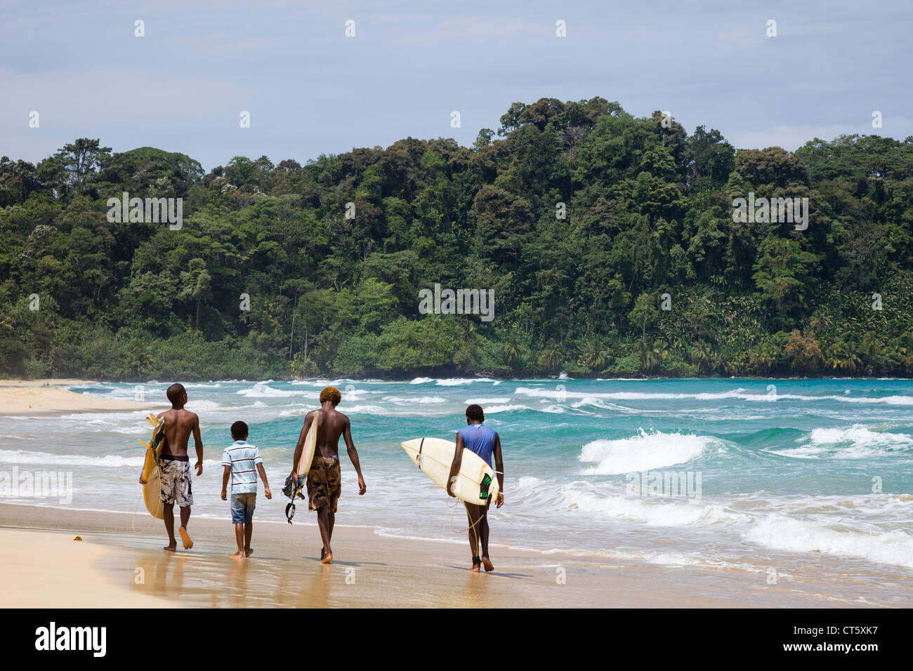 Surfers camminando lungo il mare in spiaggia Wizard (prima spiaggia) su Isla Bastimentos, Bocas del Toro, Panama. Foto Stock
