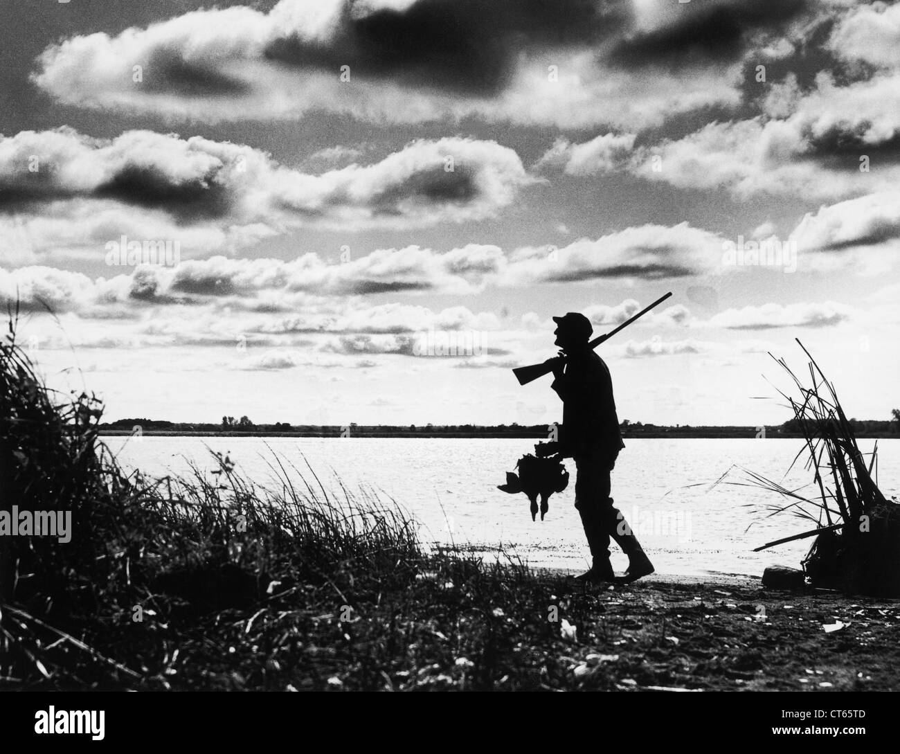 Silhouette di un cacciatore di anatre passeggiate lungo il lago Foto Stock