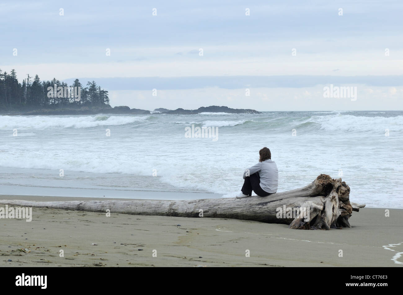 Giovane donna seduta sul tronco di albero sulla spiaggia a tofino area sull isola di Vancouver Foto Stock