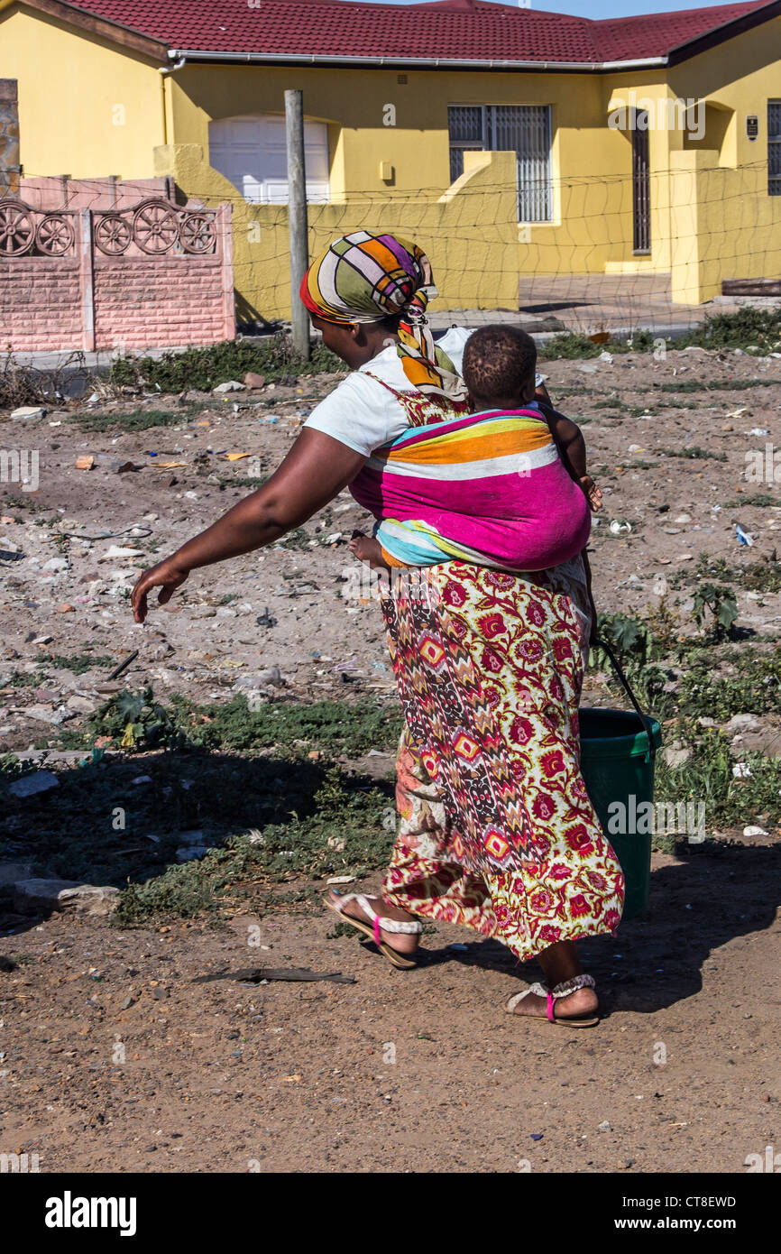 Una donna con un bambino sulla schiena preleva acqua da un rubinetto comunale in Langa borgata africana nei pressi di Città del Capo, Sud Africa Foto Stock