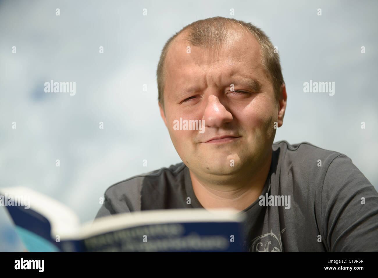 Giovane uomo la lettura del libro scientifico contro lo sfondo del cielo Foto Stock