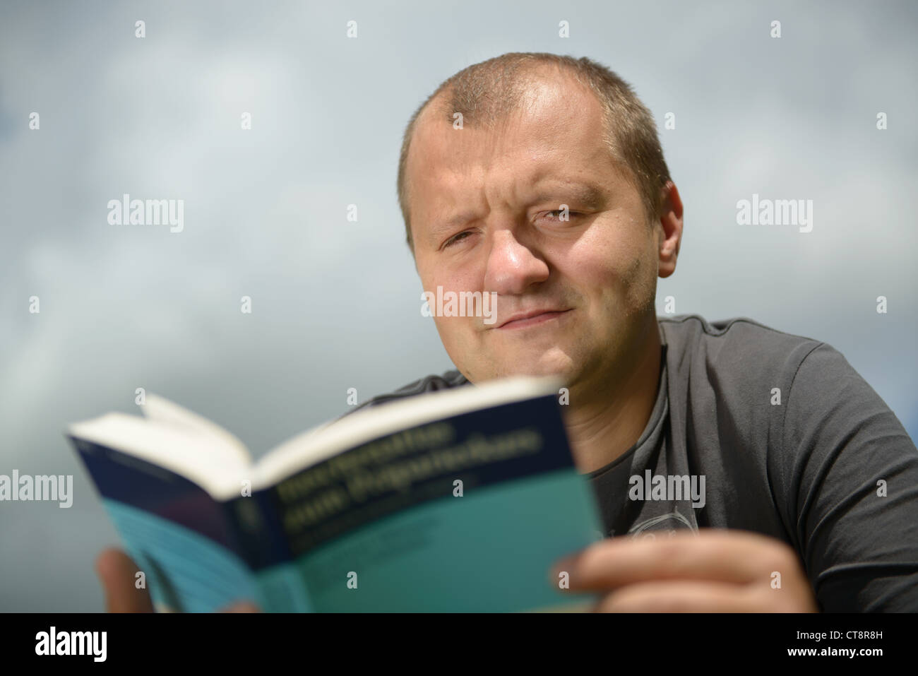 Giovane uomo la lettura del libro scientifico contro lo sfondo del cielo Foto Stock