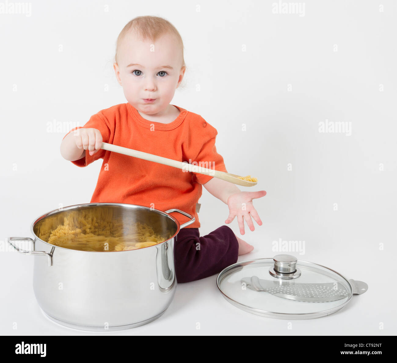 Bambino con grande pentola di cottura e il cucchiaio di legno in sfondo grigio neutro Foto Stock