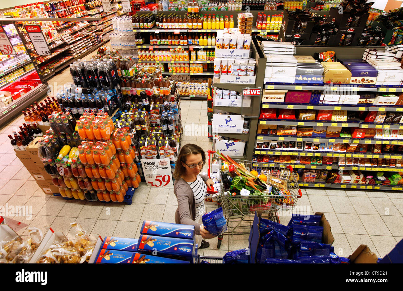 La donna è lo shopping in un grande supermercato. Passeggiando tra i rack, riempito con diversi prodotti alimentari. Foto Stock