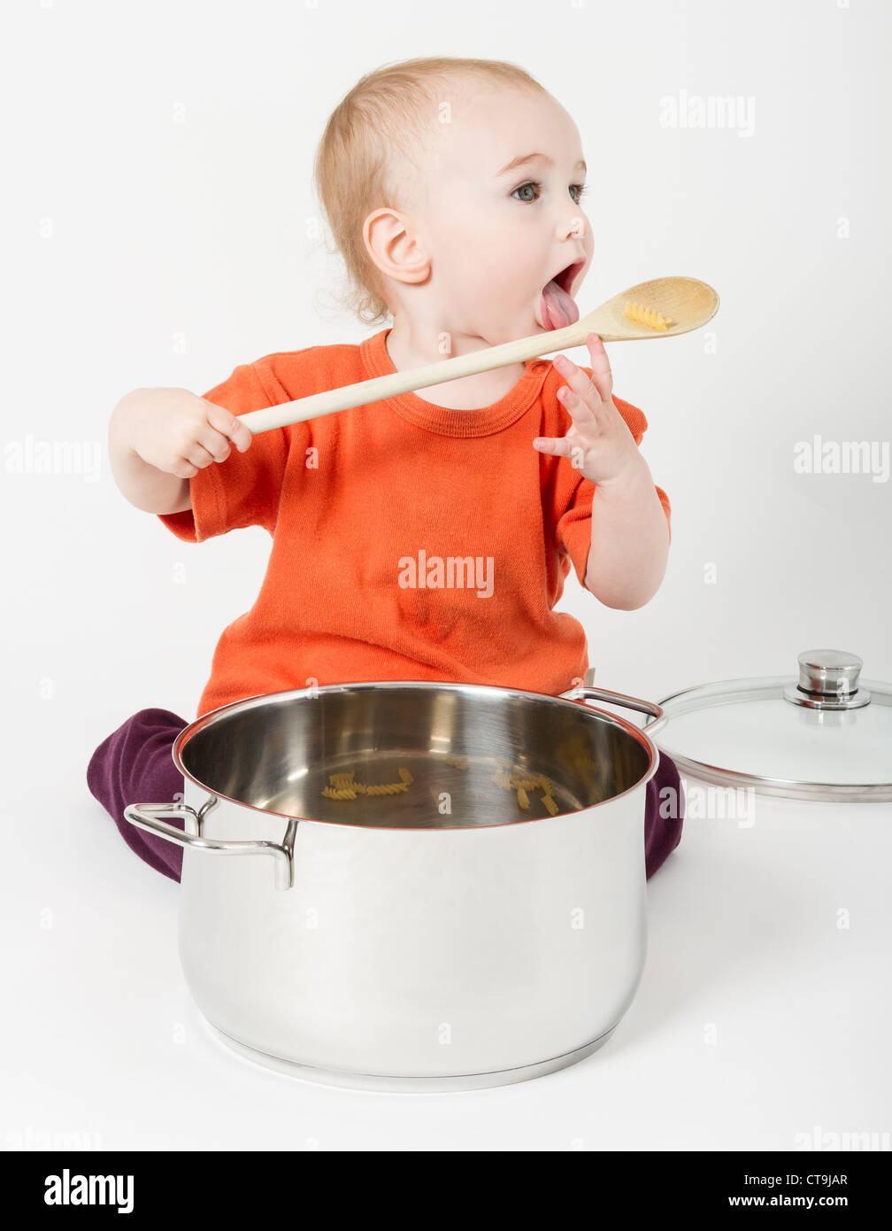 Bambino con grande pentola di cottura e il cucchiaio di legno su sfondo grigio neutro Foto Stock