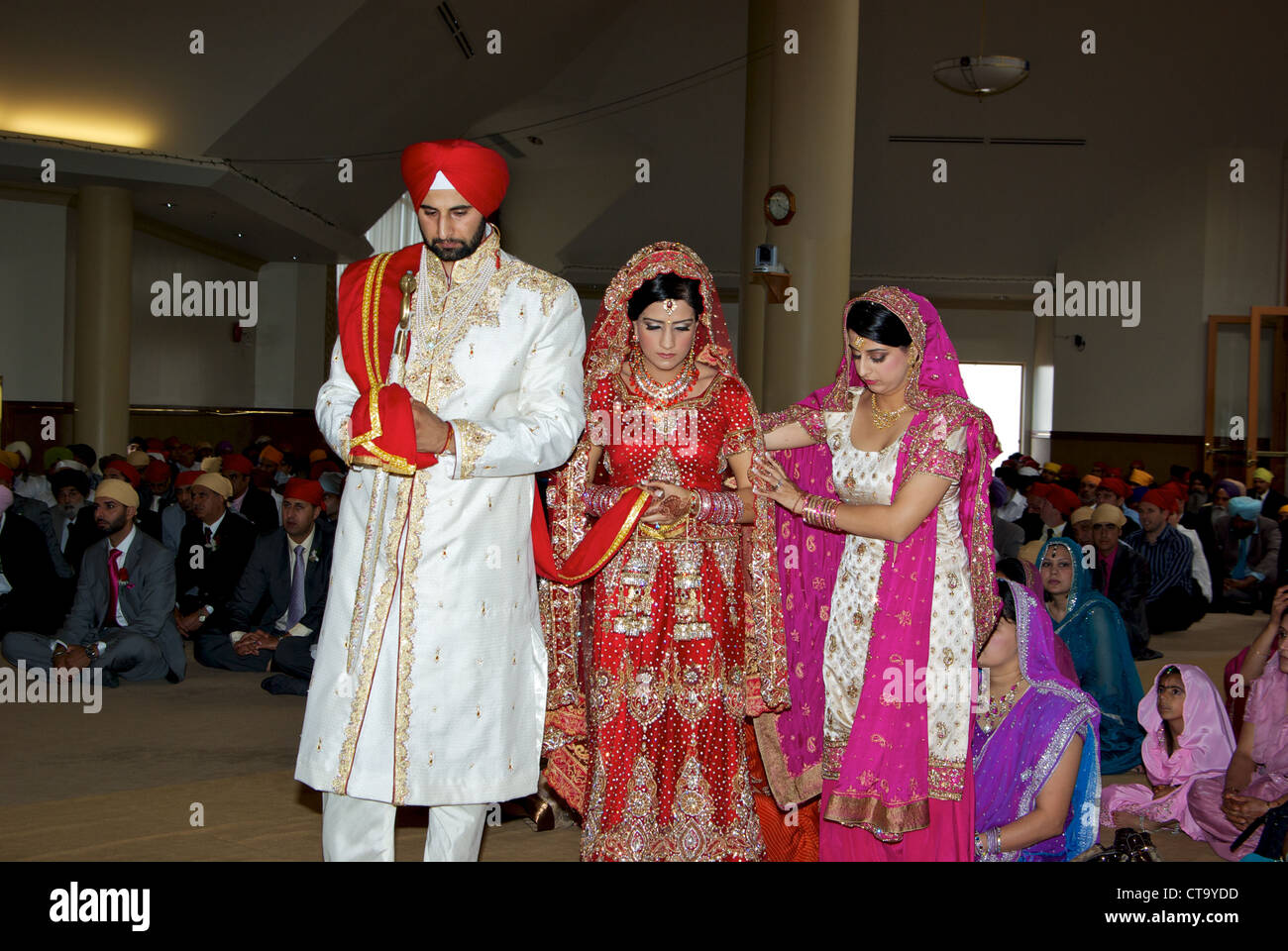 Tradizionale East Indian wedding groom luminoso turbante rosso sposa leader sari rosso intorno al tempio sikh altare uniti matrimonio sciarpa Foto Stock