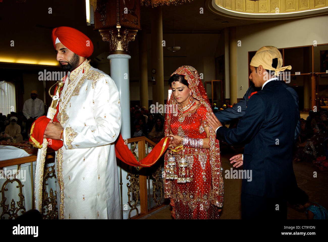 Tradizionale East Indian wedding groom indossando luminoso turbante rosso sposa leader intorno al tempio sikh altare uniti matrimonio sciarpa Foto Stock