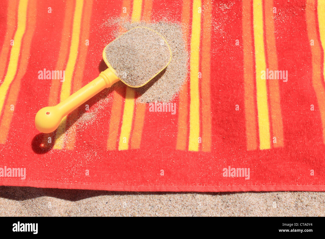 Giallo pala di plastica piena di sabbia spiaggia versato sul tovagliolo colorato Foto Stock