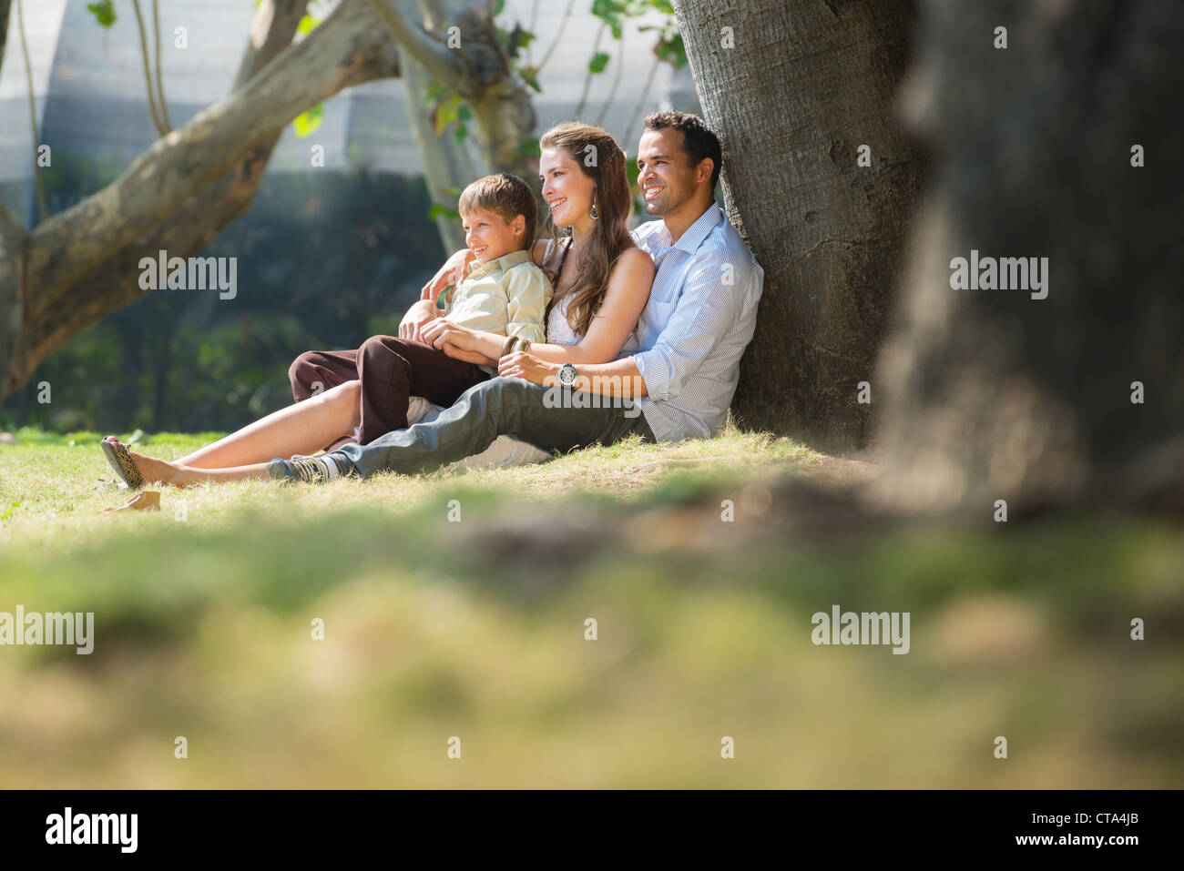 La famiglia felice con l'uomo, donna e bambino appoggiato su albero nel parco della città. Spazio di copia Foto Stock