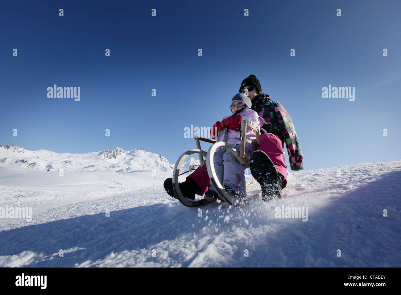 Due ragazze, 12 e 2 anni, slitta verso il basso di una collina su un tobogan, slitta, Kloesterle, Arlberg, Austria Foto Stock