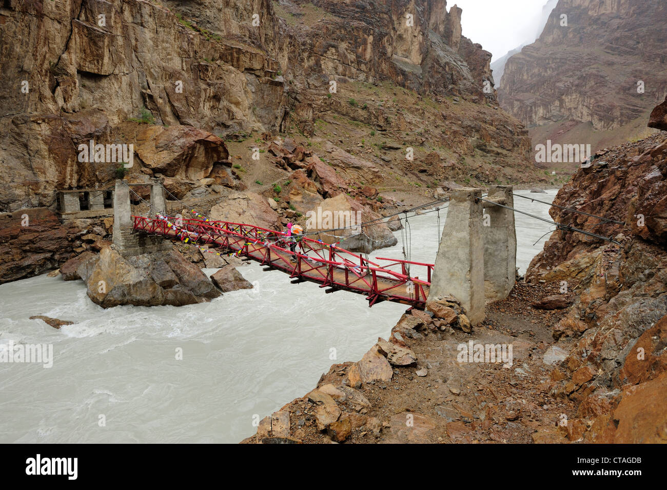 Donna Varcando il fiume sul ponte di sospensione vicino al monastero di Phuktal, Phuktal, Zanskar gamma traversa, Zanskar Range, Zanskar, Ladak Foto Stock