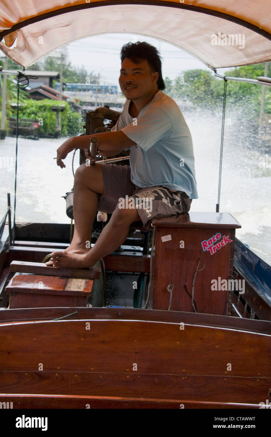 Un capitano al timone di una lunga coda di barca su Bangkok Yai canal a Bangkok, in Thailandia Foto Stock