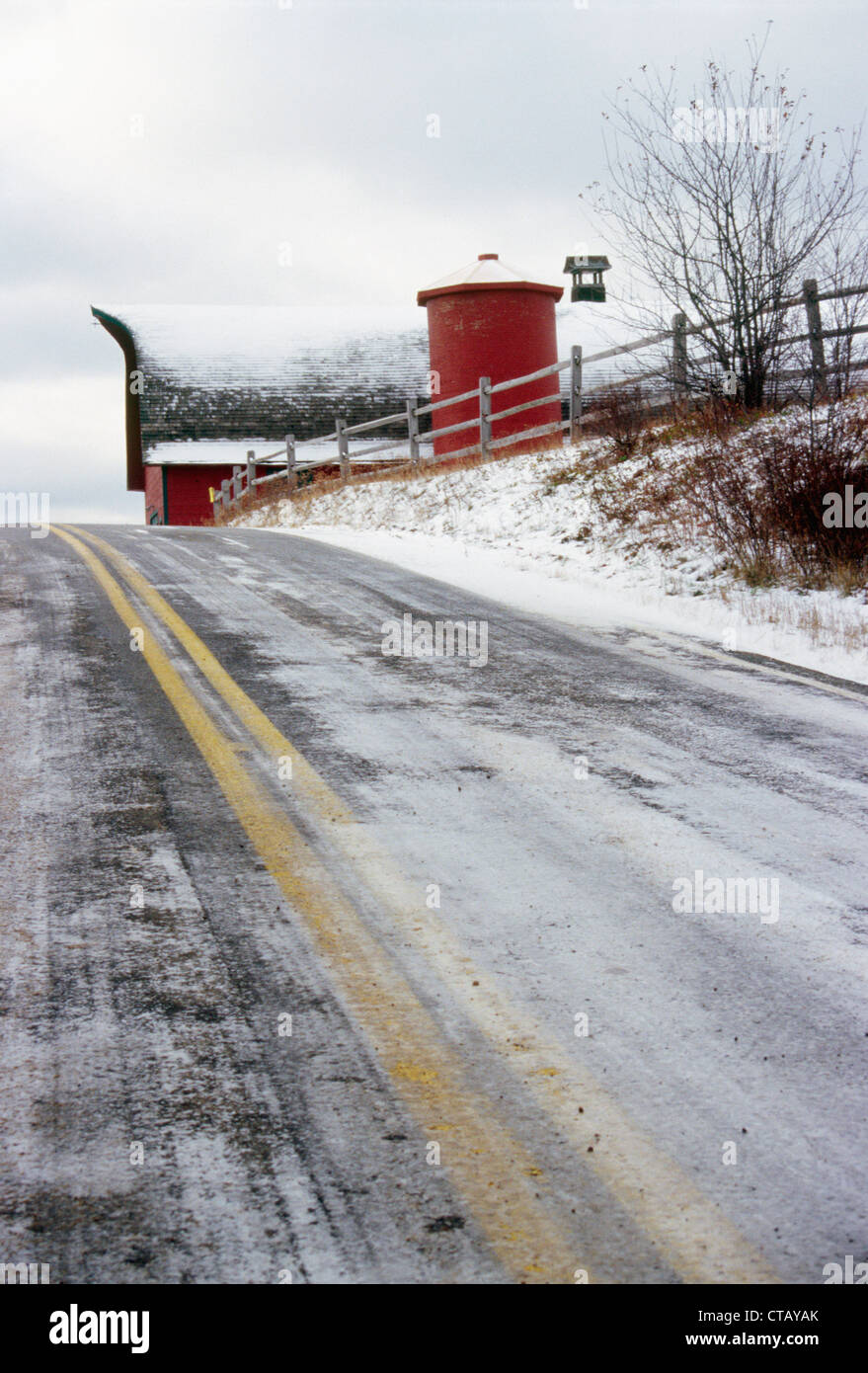 Una coperta di neve strada con un fienile in background. Foto Stock