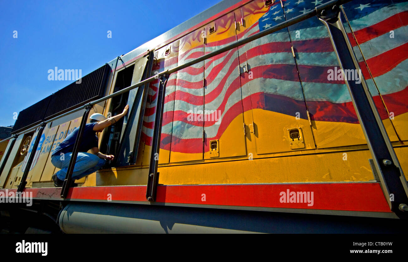 Un meccanico funziona su una locomotiva diesel in Roseville, CA, cantieri ferroviari, nota ondeggianti bandiera americana. Foto Stock