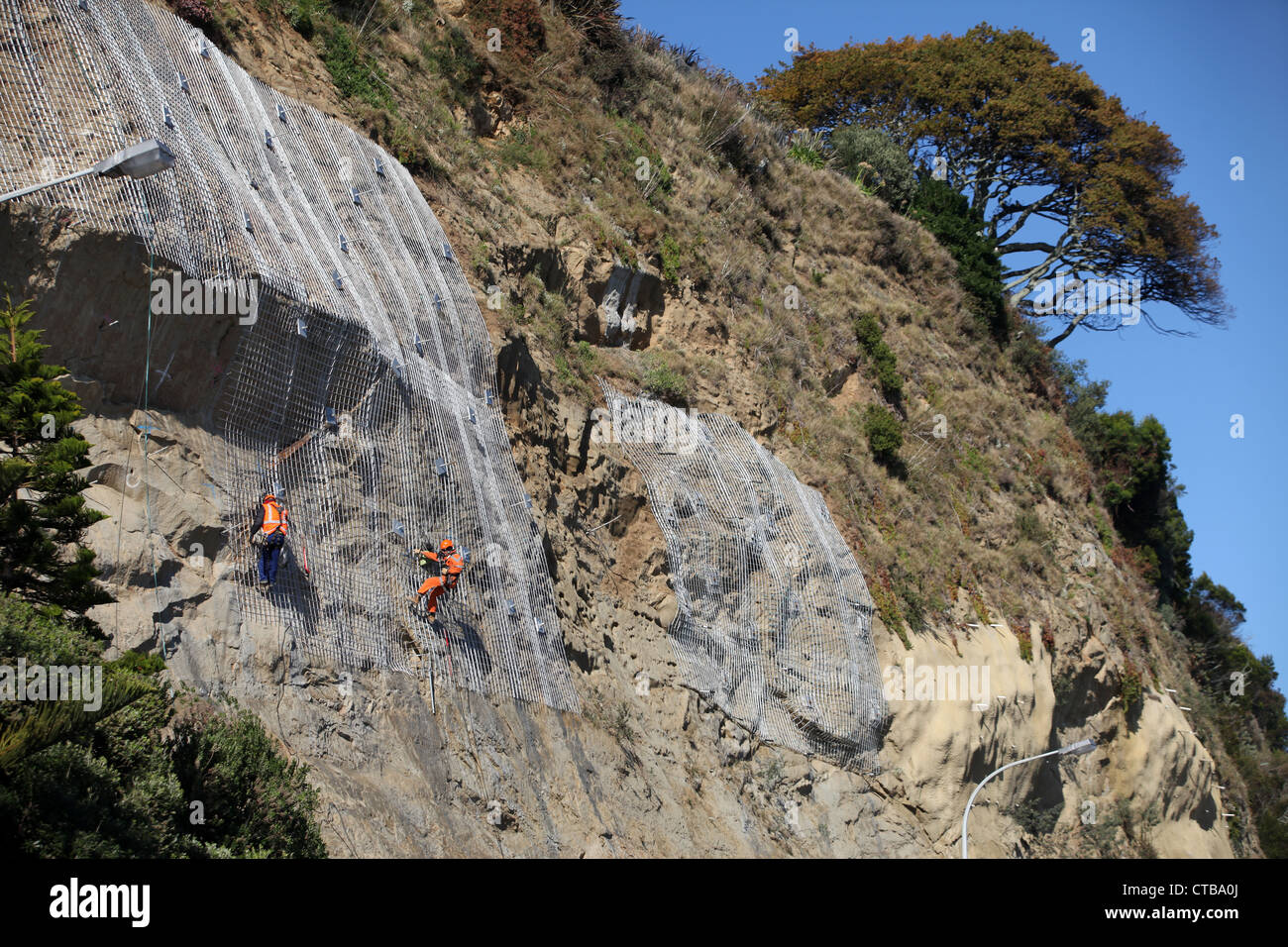 La discesa in corda doppia lavoratori edili luogo maglia di filo su rocce instabili in Nelson, Nuova Zelanda Foto Stock