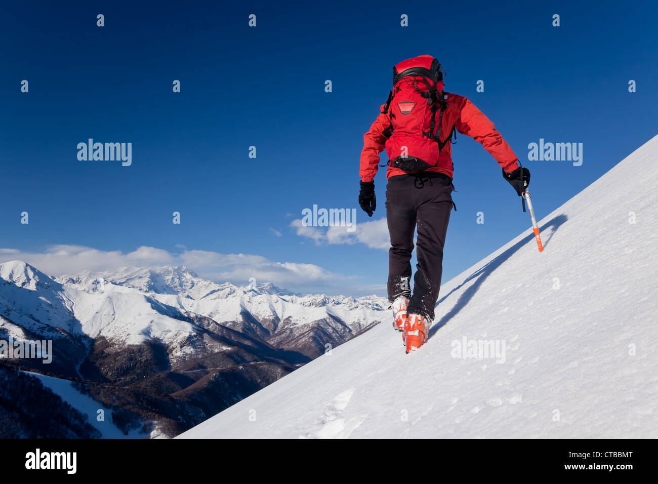 Un maschio di scalatore vestito di rosso si arrampica verso il basso pendio nevoso inverno cielo chiaro giorno sullo sfondo il Monte Rosa massiccio Italia Europa Foto Stock