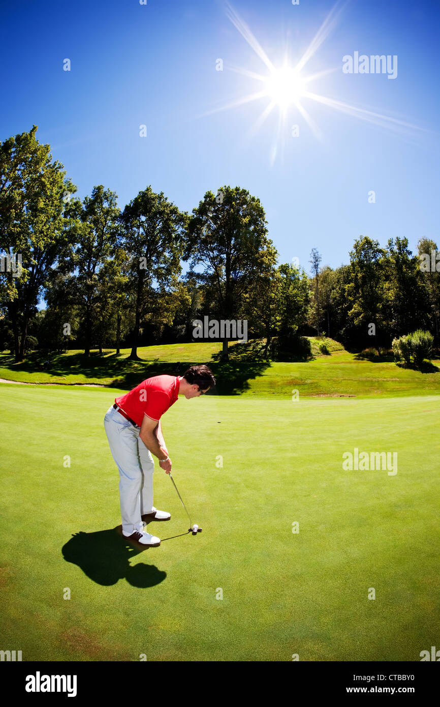 Un giovane maschio bianco golfista maglietta rossa mutanda bianca passa per il verde su fairway telaio verticale chiara giornata estiva back-light Foto Stock