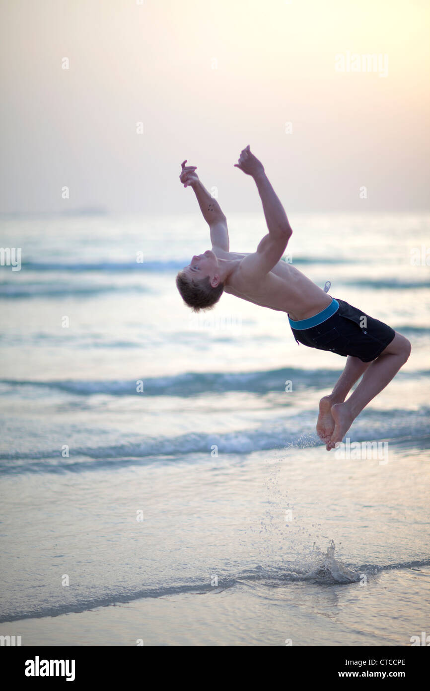 16 anno vecchio ragazzo fare back flip sulla spiaggia. Foto Stock