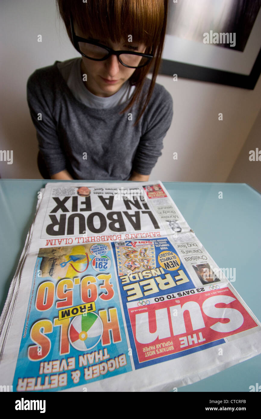 Una giovane donna legge l'edizione britannica del quotidiano The Sun a un tavolo, illustrando i lettori dei tabloid britannici, l'impegno dei giovani con la stampa popolare e il consumo occasionale dei media in un ambiente rilassato di tutti i giorni Foto Stock
