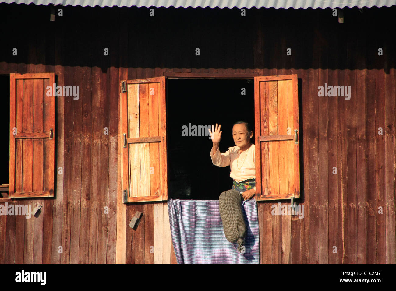 Donna birmani guardando fuori di casa stilt finestra, Lago Inle, stato Shan, Myanmar, sud-est asiatico Foto Stock