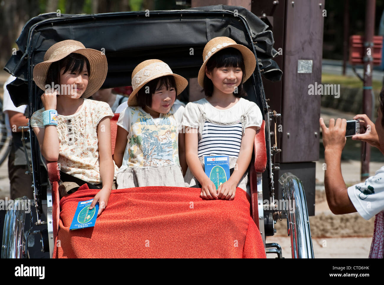 Tre bambini giapponesi che indossano cappelli da sole di paglia hanno la loro foto scattata mentre siedono in un risciò (Nara, Giappone) Foto Stock
