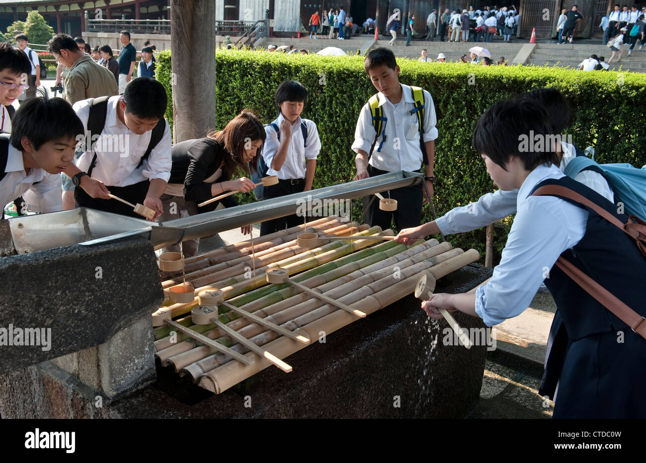 Studenti giapponesi che eseguono il rituale di temizu (purificazione) prima di entrare nel tempio buddista di Todai-ji, a Nara, Giappone. Foto Stock