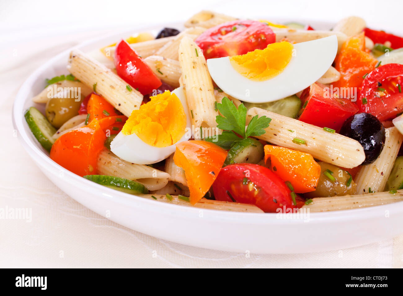 Una ciotola di insalata di pasta con uova, pomodori, cetrioli, arancio pepe e le olive in un condimento di erbe. Foto Stock