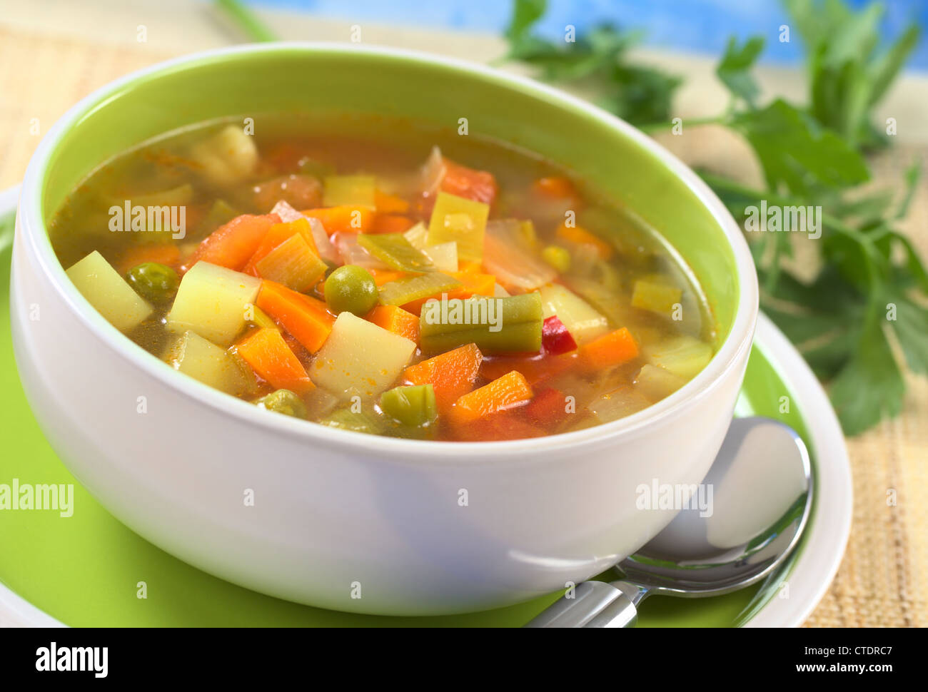 Verdura fresca zuppa di verde fagiolo, pisello, carota, patata, il peperone rosso, il pomodoro e il porro nella ciotola con il prezzemolo nel retro Foto Stock