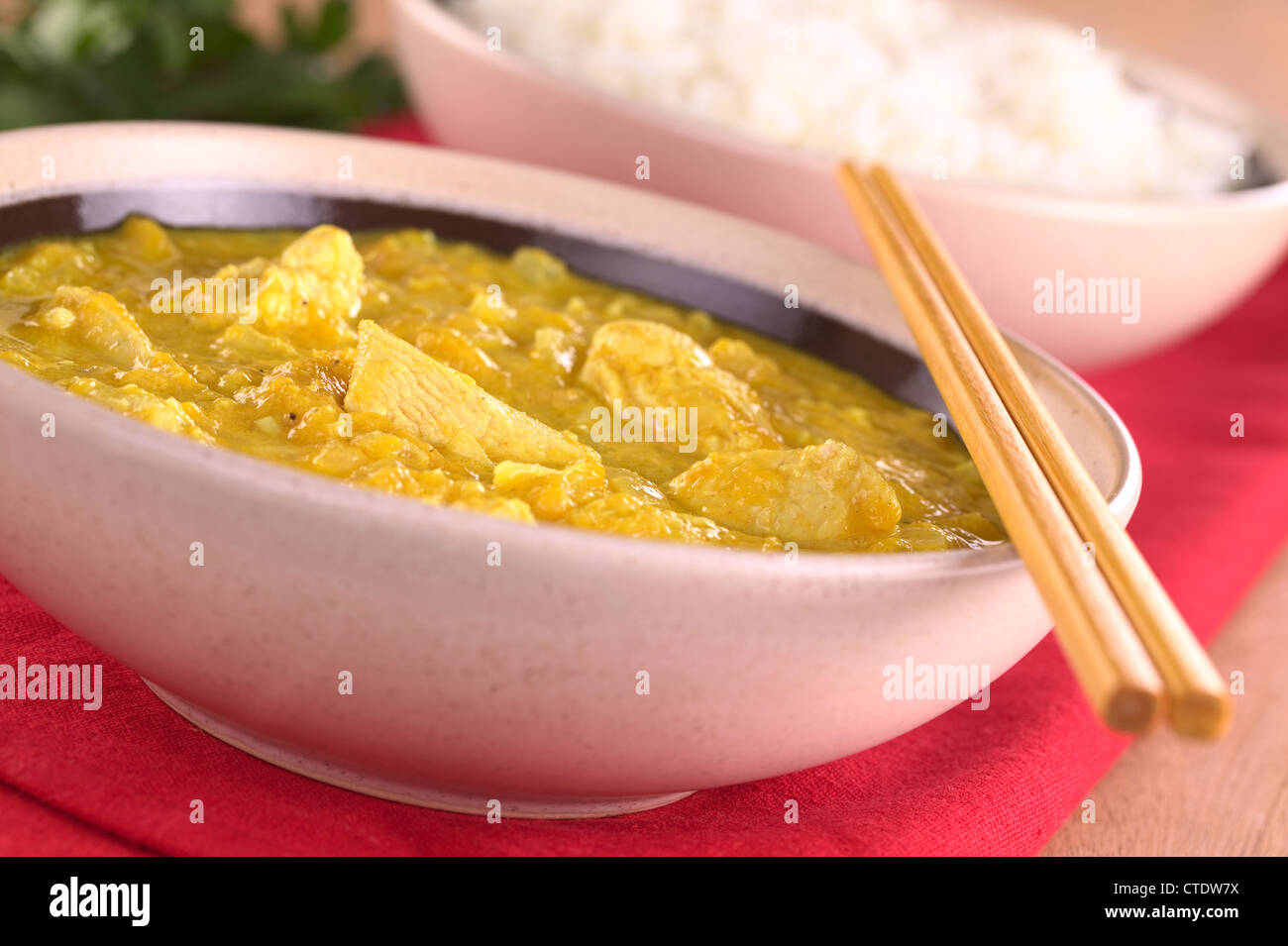 Pollo-mango curry con riso in retro (messa a fuoco selettiva, concentrarsi su i pezzi di pollo nella parte anteriore) Foto Stock
