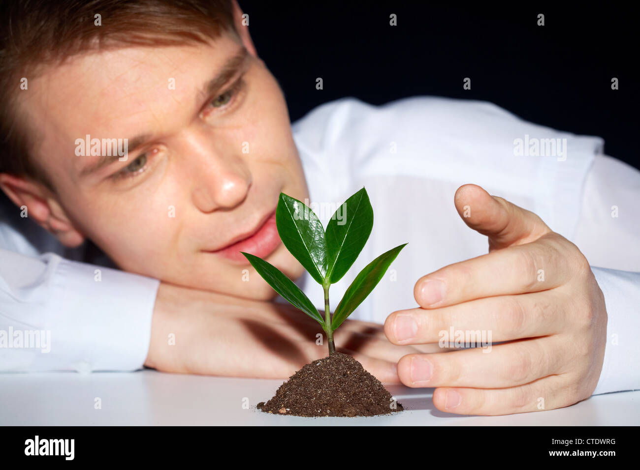 Caring giovane uomo proteggere germoglio verde da condizioni avverse Foto Stock