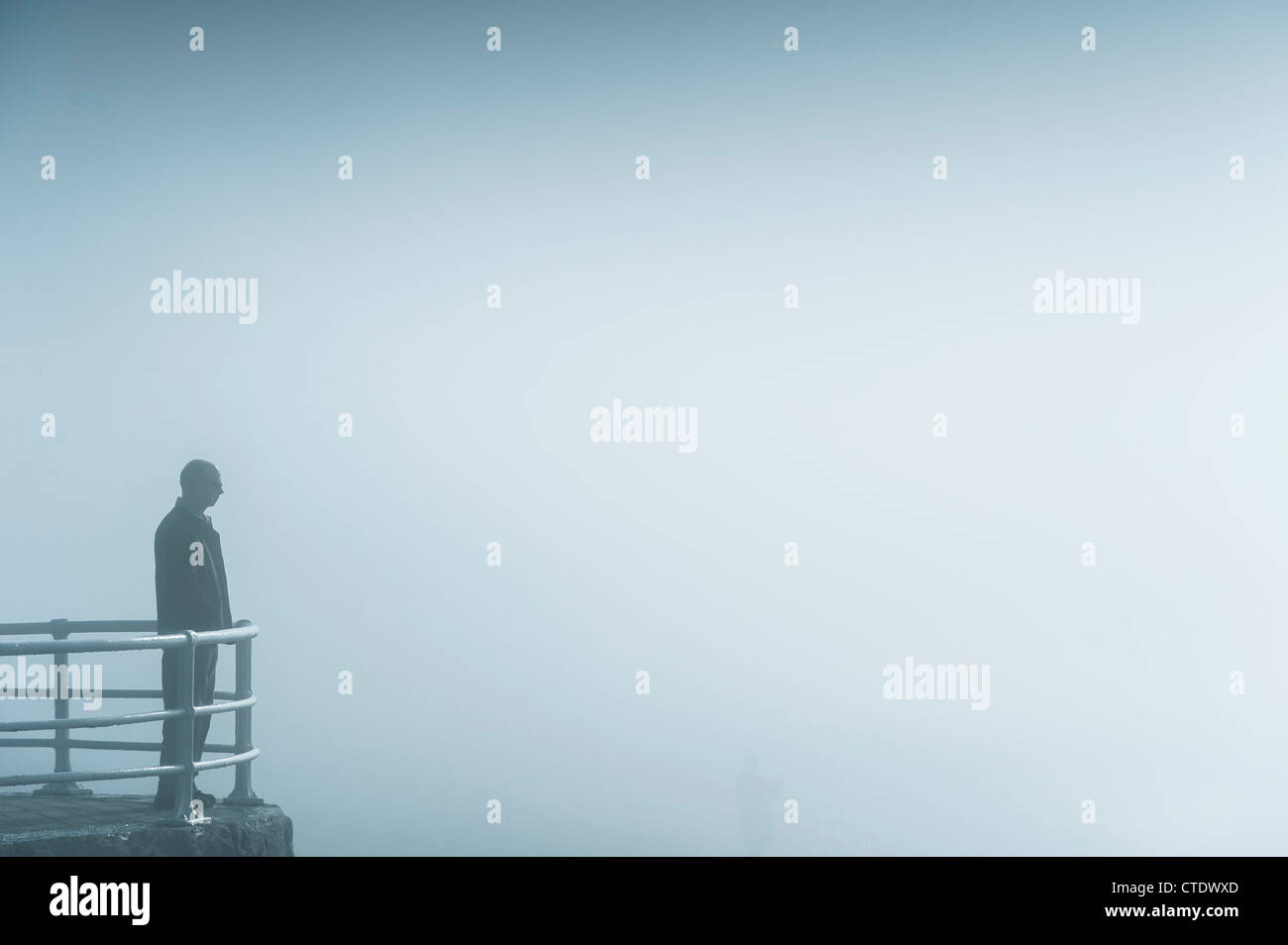 Un uomo in piedi da sola nella nebbia foggy nebbia misty meteo Regno Unito - lungomare ringhiere con spazio copia a destra Foto Stock