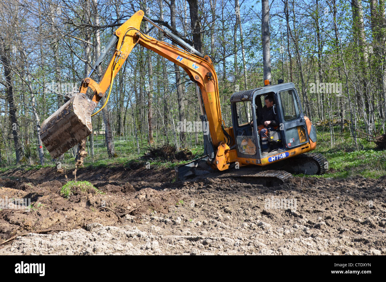 Escavatore sono scavare in un campo in primavera Foto Stock