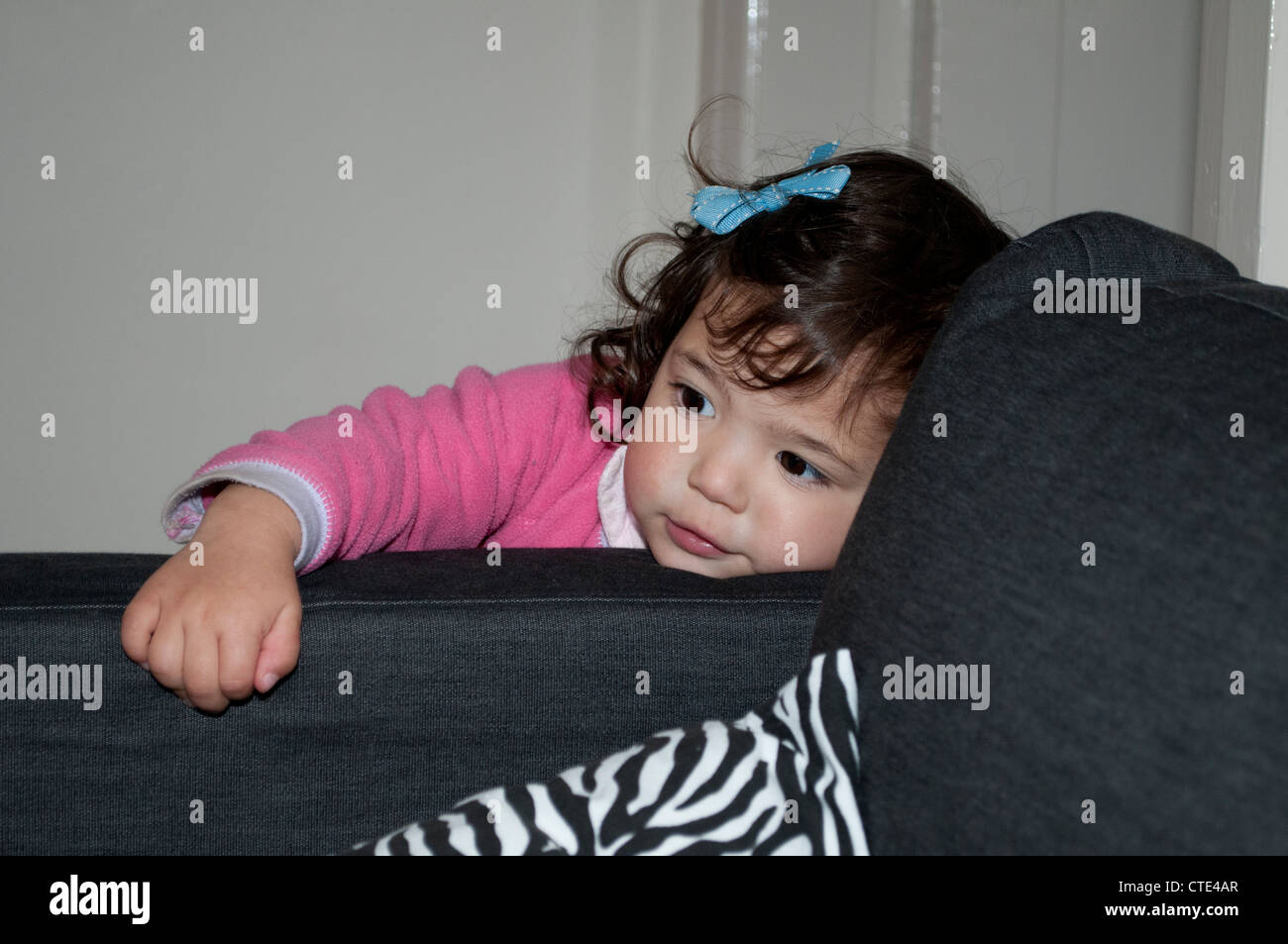 Bambina con fiocco blu appoggiata su un divano Foto Stock