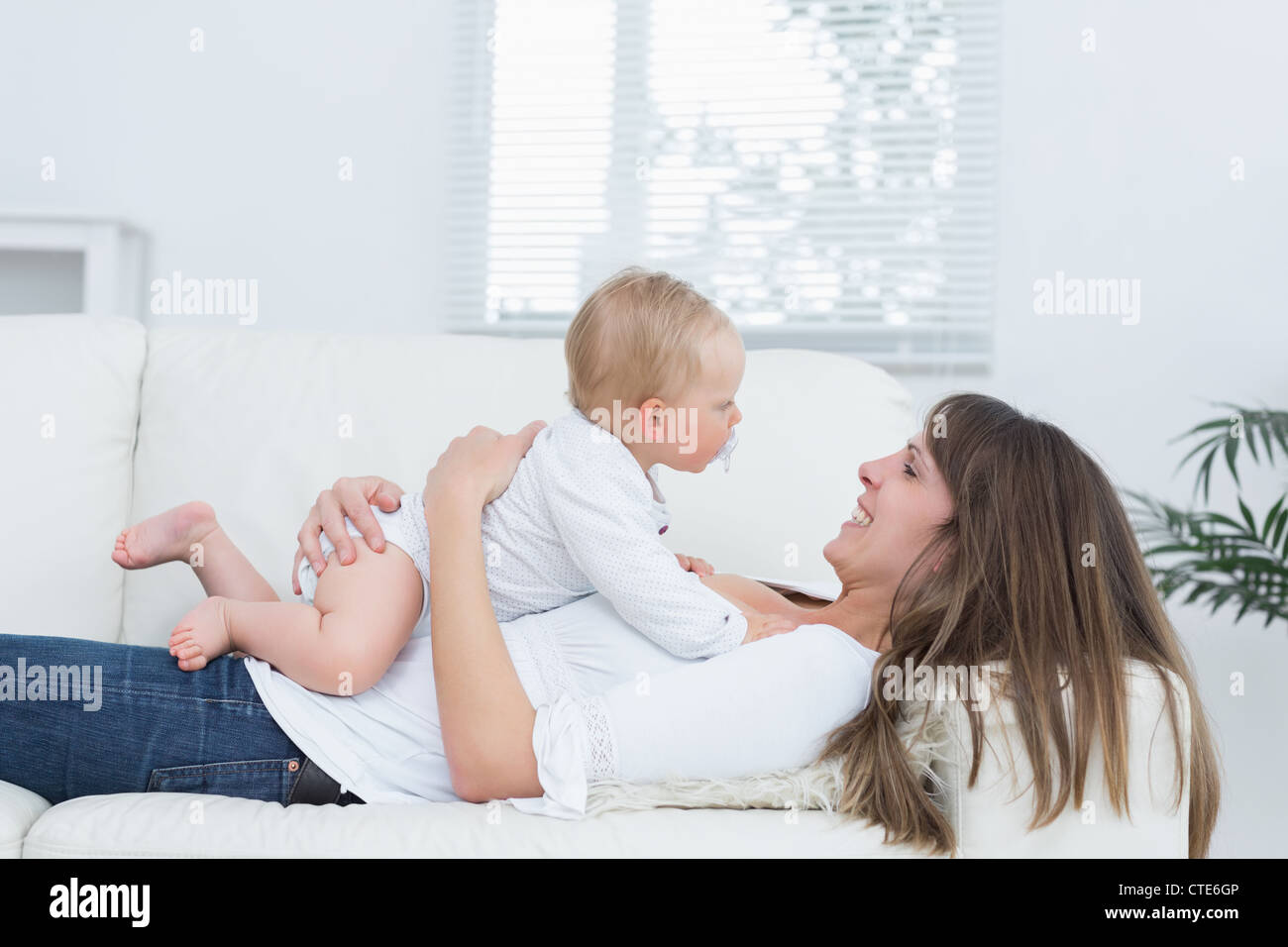 Madre giacente su un divano tenendo un bambino sul suo petto Foto Stock
