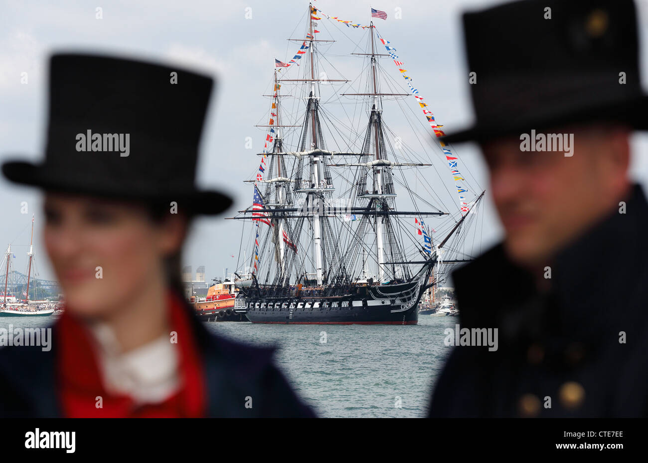 US Coast Guard marittimi in 1812 uniformi stand su un molo come la USS Constitution, centro di sfondo, vele nel porto di Boston Foto Stock