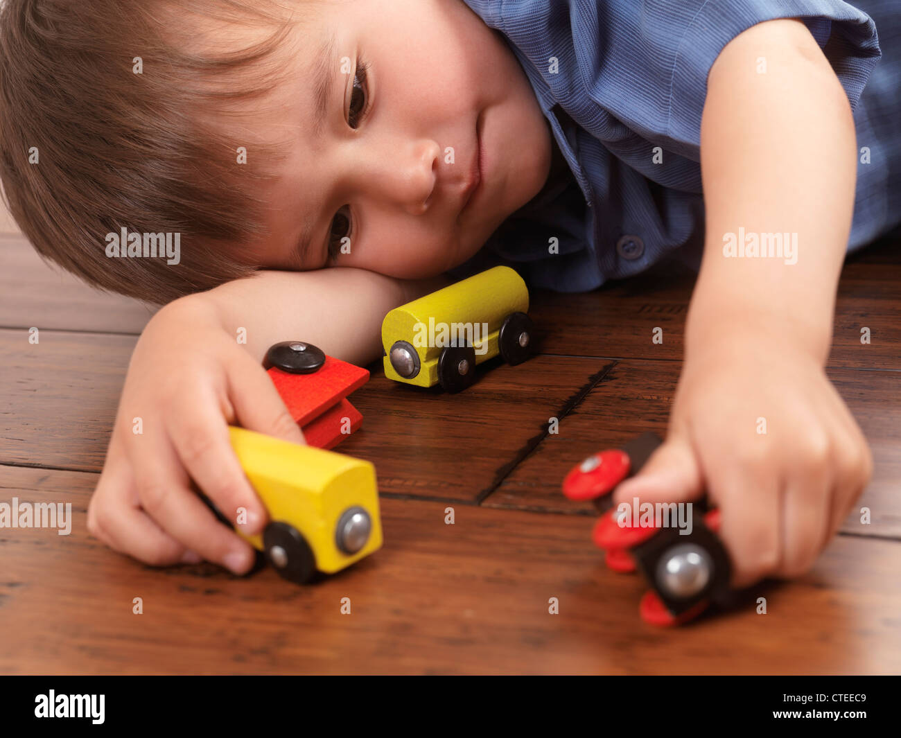 Due anni di vecchio ragazzo giocando con un coloratissimo giocattolo di legno treno su pavimento in legno duro Foto Stock