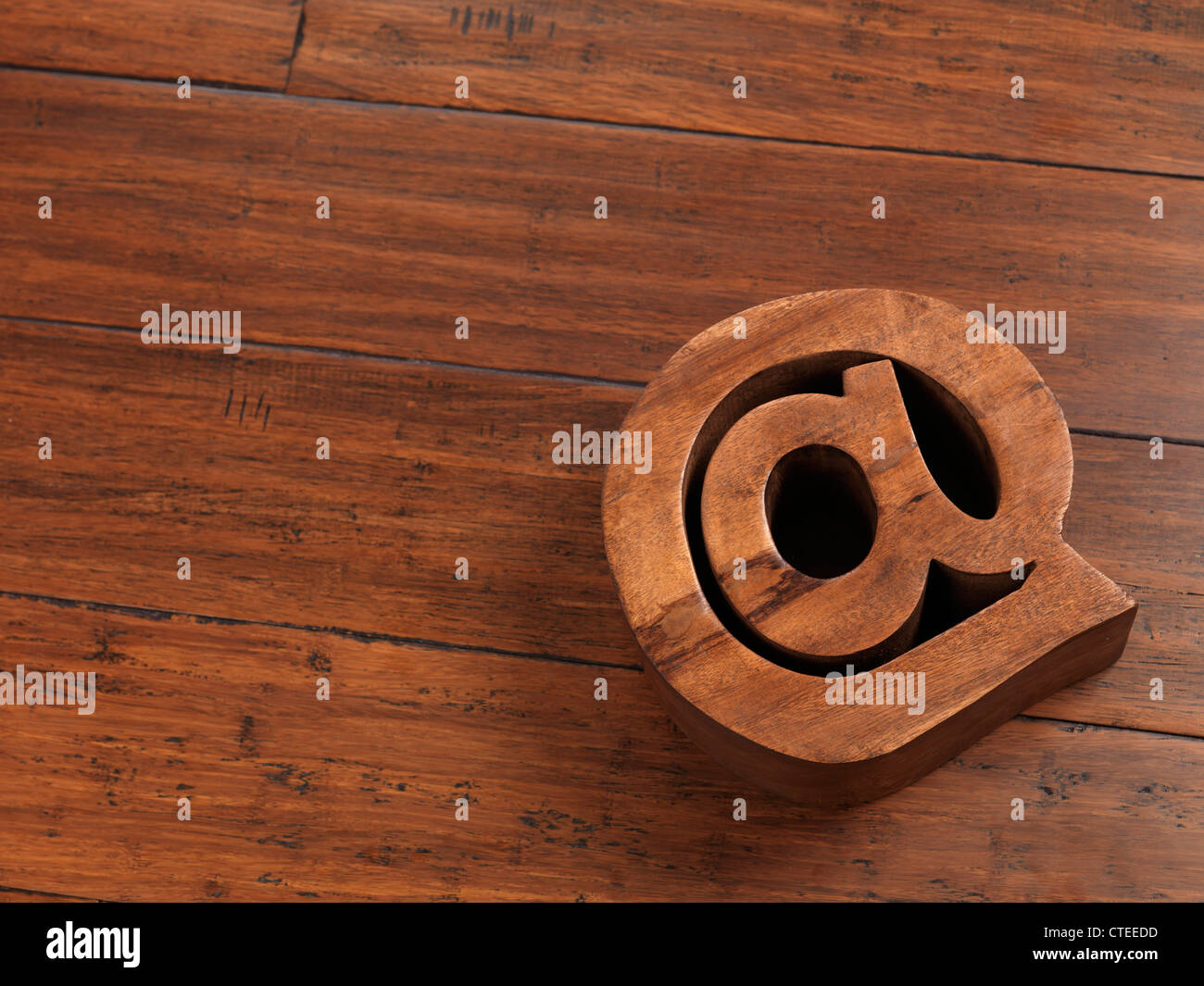 Indirizzo di posta elettronica il simbolo a @ fatta di legno che giace sul piano hardwwod sfondo Foto Stock