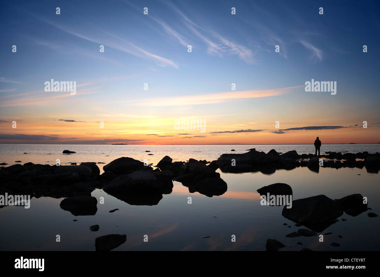 Un uomo sulle pietre costiere con protagonista presso il luminoso tramonto sul mare Foto Stock