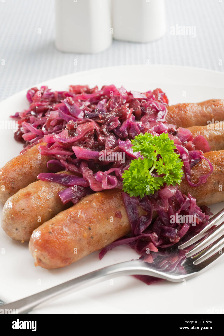 Il tedesco Thuringer o salsicce bratwurst, speziato con cavolo rosso con Apple, su una piastra con una forchetta. Foto Stock