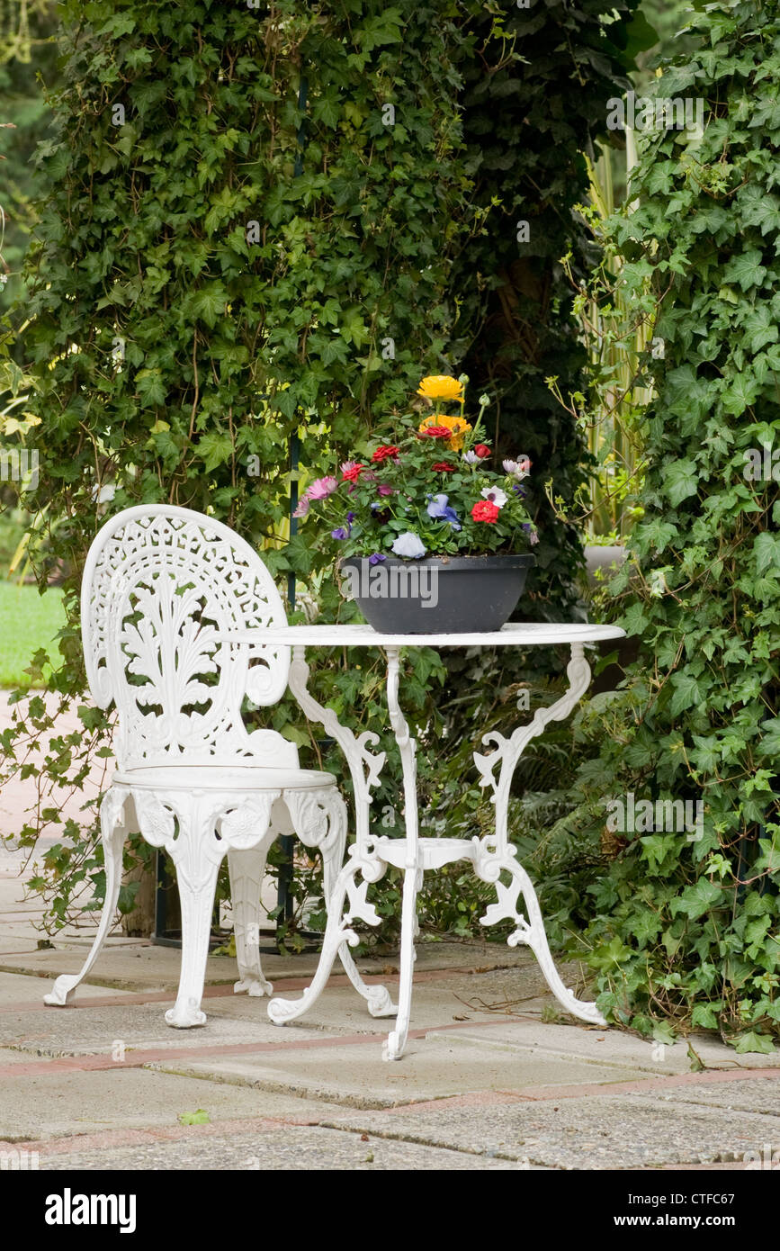 Un bianco di ferro battuto tavolo e sedia a sedersi in un ambiente da giardino Foto Stock