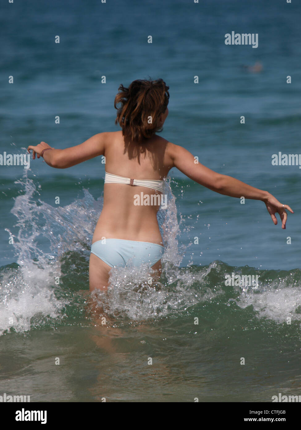 Giovane donna che vengono spruzzati da una piccola onda, Newquay, Cornwall, Regno Unito Foto Stock
