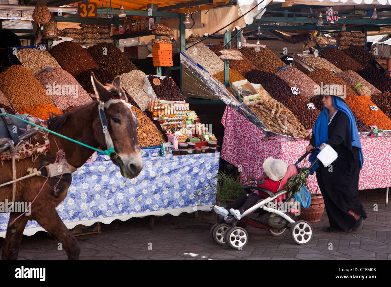 Il Marocco Marrakech chiamato Piazza Djemaa El Fna. Donna e bambino buggy passando i dadi in stallo. Asino. Foto Stock