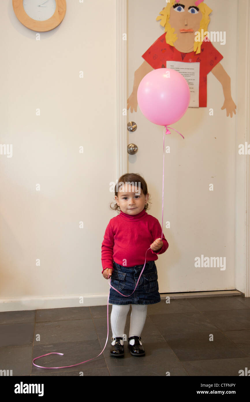 Una piccola ragazza in casa tenendo un palloncino. Foto Stock