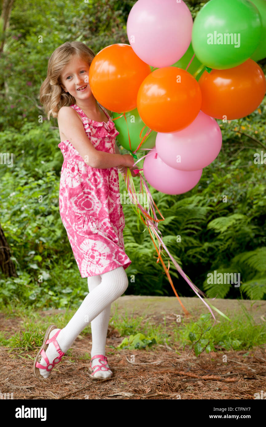 Una piccola ragazza in un abito rosa è in possesso di alcuni di palloncini colorati. Foto Stock