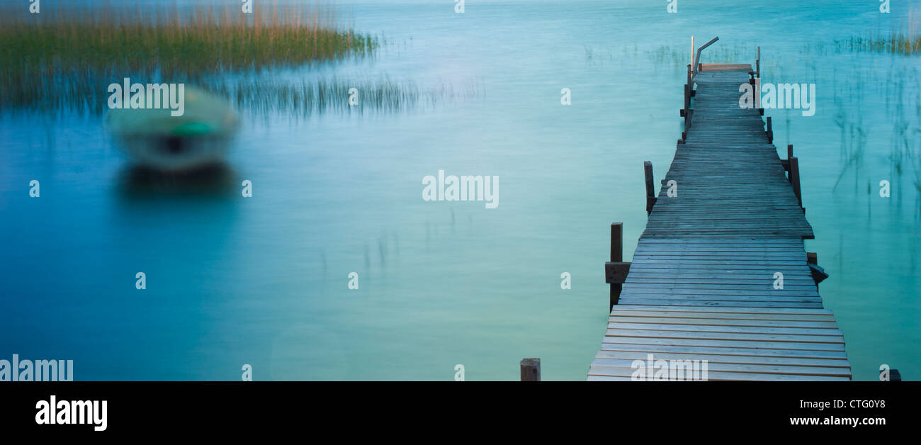 Barca bobbing sull'acqua in un lago vicino ad un pontile in legno Foto Stock
